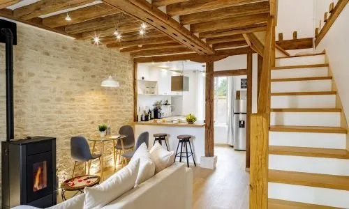 Pièce rénovée avec mur en pierre, poutres apparentes, cuisine ouverte et escalier